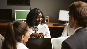 woman leading a meeting around a table with laptops